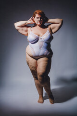 vertical image of plus size caucasian woman in lingerie with cellulite posing confident, hard light