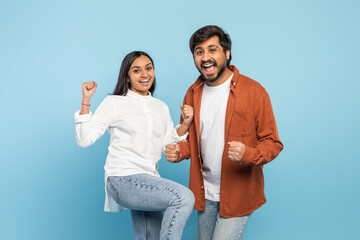 Excited couple celebrating with fists pumped on blue background