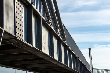 Close-up view of the steel structure of a modern bridge. Close-up of metal fence on the street. Detail of a steel bridge with blue sky in the background.