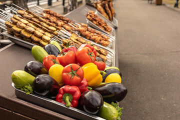 Street food stall. Fresh beautiful vegetables, tomatoes, bell pepper, zucchini , aubergine, roasted chicken , chicken and vegetables grilled on skewers close up