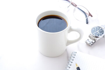コーヒーを飲みながら、リング式のメモ帳とペンでデスクワークをしているイメージ
