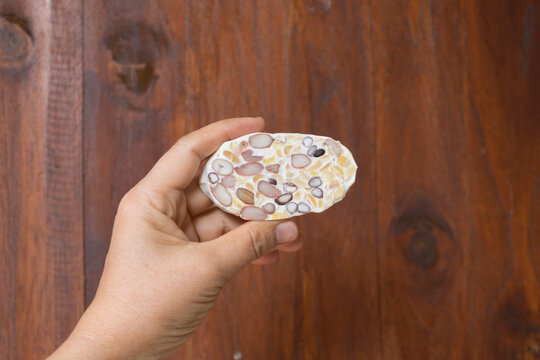 Mixed beans sliced raw Tempeh, Tempe, in woman hand on brown wooden background, closed up