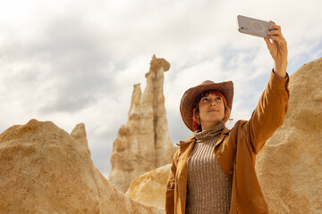 A woman in a brown jacket and hat is taking a picture of a mountain. The photo has a rustic, adventurous feel to it