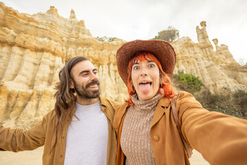 A man and a woman are posing for a picture in front of a large rock formation. The man is wearing a...