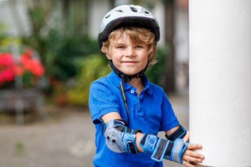 Portrait of little school kid boy in safety protection clothes scating with rollers. Active sporty...