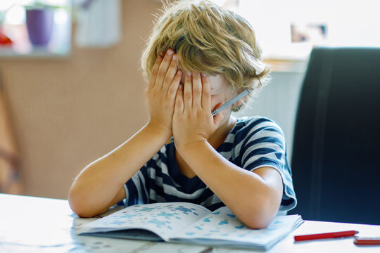 Portrait of tired upset boy doing homework in kitchen at home. Elementary school studing writing and learning. Sad and angry child.