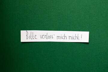 Bitte verlass mich nicht auf einem weißen Zettel auf farbigem Untergrund handschriftlich 