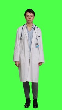 Front view Physician saying no and showing negative reaction symbol in studio, wearing a white coat and standing against greenscreen backdrop. Woman medic feeling displeased, rejection sign. Camera A.