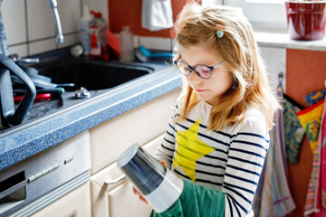 Little girl wiping plate with towel in kitchen, drying dishes. child helping at home