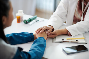 Closeup image of pediatrician reassuring sick teenage girl, touching her hands