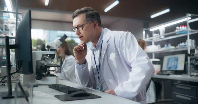 Team of Diverse Male and Female Medical Research Scientists Work on a New Generation Medical Products in a Modern Laboratory. Focus on an Adult Scientist Working on Computer, Browsing Research Data