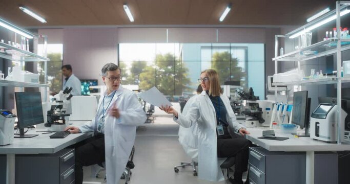 Establishing Footage of a Group of Scientists in White Lab Coats Walking in Workplace, Sitting Behind Desks and Using Computers. Young Creative People Working in a Research Laboratory