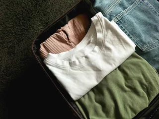 Fotobehang Close up of packed suitcase with clothes on dark carpet. Travel concept. © Nestudio