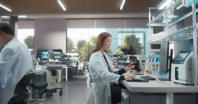 Medical and Bioengineering Research Science Laboratory with Diverse Men and Women at Work. Zoom In on an Asian Female Bacteriology Researcher Analyzing a Petri Dish with Genetic Experiment Samples