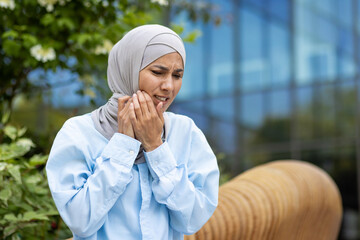 Portrait of woman wearing hijab and light blue shirt while touching cheek with both hands on...