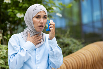 Shocked arabic woman covering neck with hand and holding bronchial asthma inhaler while having walk outdoors. Scared lady suffering from seasonal allergy and feeling hard to breath without medicine. - obrazy, fototapety, plakaty