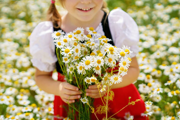 Closeup of little preschool girl in daisy flower field. Cute happy child in red riding hood dress play outdoor on blossom flowering meadow with daisies. Leisure activity in nature with children.