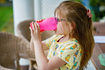 Girl holding glass with water. Happy child at summer