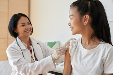 Smiling pediatrician wiping injection site on girls arm