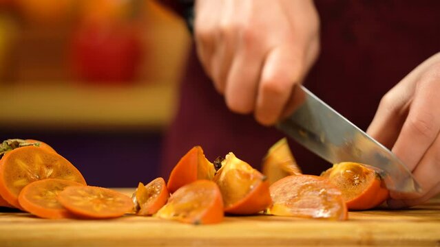 Cutting into pieces of ripe orange persimmon. Man cutting fresh kinglet fruit. Sliced persimmon on board.
Organic fruit.