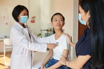 Teenage girl looking at mother when doctor listening to her breath