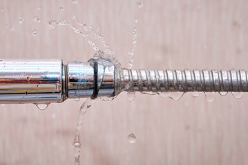Laaking water hose close to shower head, water flow from the hole of the hose closeup. Broken shower hose, bathroom leaks, common water issues in home. Leaky hoses can cause water damage.