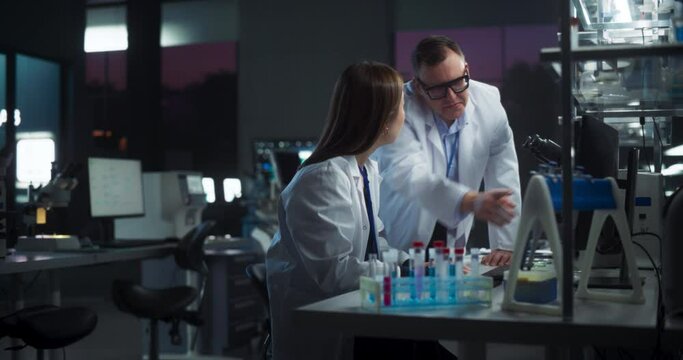 Caucasian Medical Supervisor Having a Conversation with an Asian Scientists About Gene Cloning and Other Research Projects, Genome Editing Technology. Smart Diverse Team Working in a Lab at Night