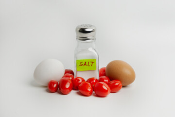Eggs, tomatoes and salt in a salt shaker on a white background. Over-salting food is harmful to health. You need to salt your food in moderation