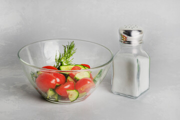 Vegetable salad and salt in a salt shaker on a white background. Too much salt in food is unhealthy. It is necessary to salt food moderately
