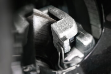 Brake disc and caliper with brake pads visible through the car's alloy wheel. Selective soft focus.