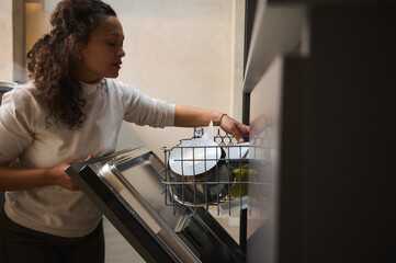 Charming multi ethnic woman loading, unloading, emptying out, putting dishes inside baskets in...