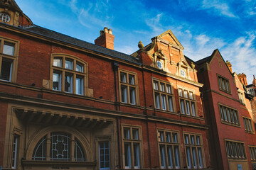 Fototapeta na wymiar Traditional red brick building with ornate windows under a clear blue sky, showcasing classic architectural details and warm sunlight casting shadows in York, North Yorkshire, England.