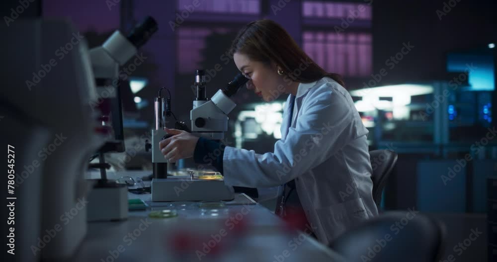 Poster Genetic Research Scientist Using Microscope in an Applied Science Laboratory in the Evening. Portrait of a Beautiful Asian Lab Engineer in White Coat Developing New Medical Products