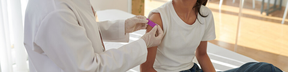 Web banner with doctor applying bandage on arm of patient after vaccination
