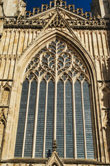 Gothic architecture detail of a cathedral window with intricate tracery and stained glass, set against a clear blue sky in York, North Yorkshire, England.