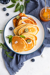 Traditional fluffy pancakes with orange jam, blueberries, coconut chips and mint for healthy breakfast, grey background. High key photography.