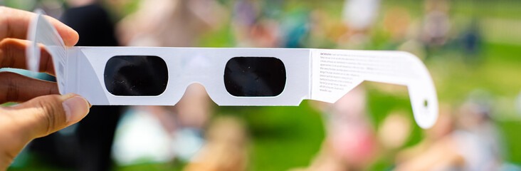 Panorama view paper optics solar eclipse glasses scratch resistant polymer lenses filter harmful ultraviolet, infrared ray, blurry crow people on grassy yard watching totality show, Dallas, Texas