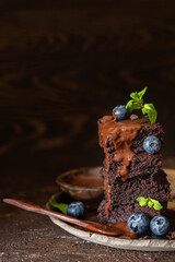 Dark chocolate brownie decorated with blueberry, mint, chocolate sauce and pieces of chocolate. Tasty homemade fudge and chewy dessert with melting chocolate.