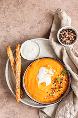 Pumpkin and carrot soup with cream, mint and seeds on brown concrete background. Traditional autumn or winter vegetarian soup with creamy silky texture.