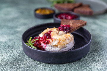 Baked camembert cheese on plate with cranberry sauce, orange jam, toasted bread with seeds and rosemary. Brie type of cheese. Italian, French cheese.