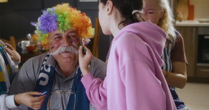 Granddaughter  draws a flag on her grandfather's face before watching the match with her family at home on TV