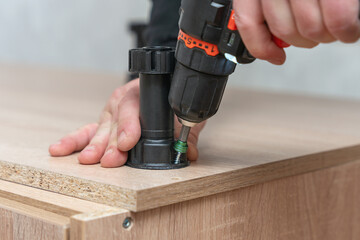 Assembling furniture, a man screws a plastic leg with a screwdriver