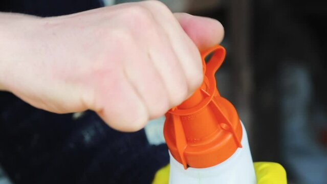 A man's hand opens a plastic bottle with a dispenser cap for mixing gasoline and oil for 2-stroke engines.