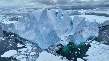Flying over giant iceberg near Ilulissat, Greenland. Iceberg pieces break off and fall into the water. Aerial arctic nature landscape, global warming and climate change concept - 780555430