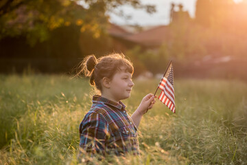 Cute little patriot sitting on the meadow and holding the national flag of United States
