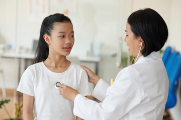 Positive pediatrician listening to heartbeat of Vietnamese teenage girl