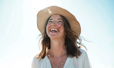 A woman in her thirties laughing on the beach, wearing white and a straw hat on a sunny day with a clear sky