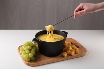 Woman dipping piece of bread into fondue pot with tasty melted cheese at white table, closeup
