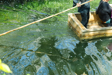 木造の小舟で客を乗せて操船する船頭の男性｜伝統的な川下りの風景