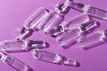 Glass ampoules with liquid on purple background, top view